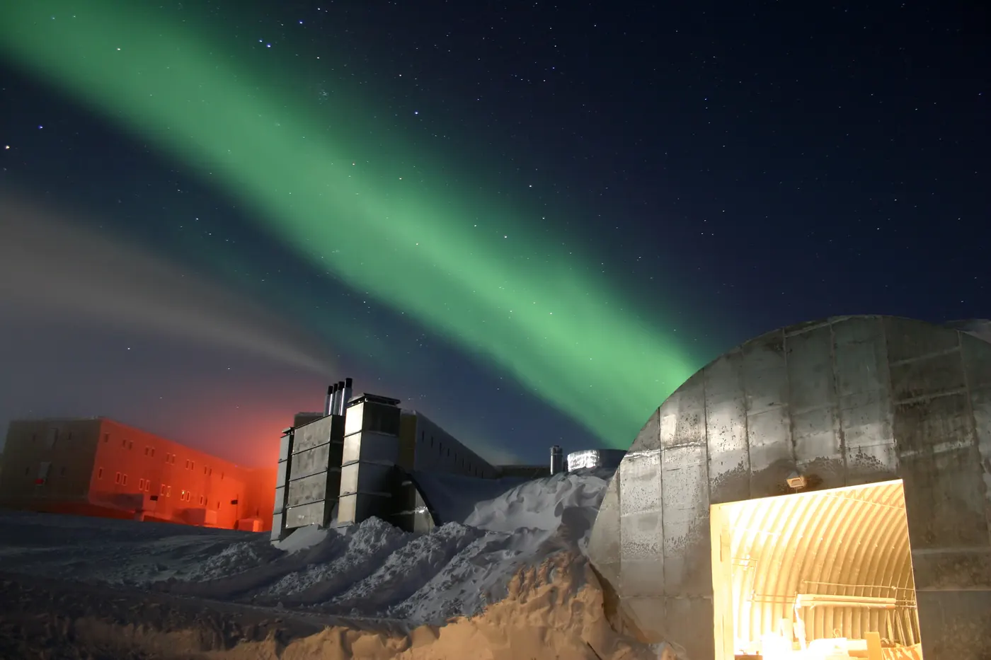 The Amundsen-Scott South Pole Station buildings illuminated against the dark Antarctic sky with green aurora australis streaking overhead