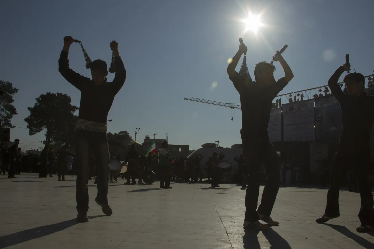 Young men in silhouette swinging chain flails during an Ashura procession