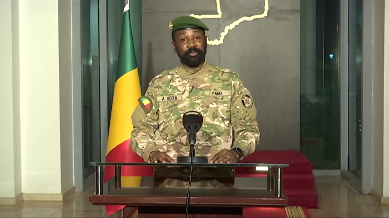 Colonel Assimi Goïta of Mali in military fatigues and a green beret, speaking at a podium beside the Malian flag