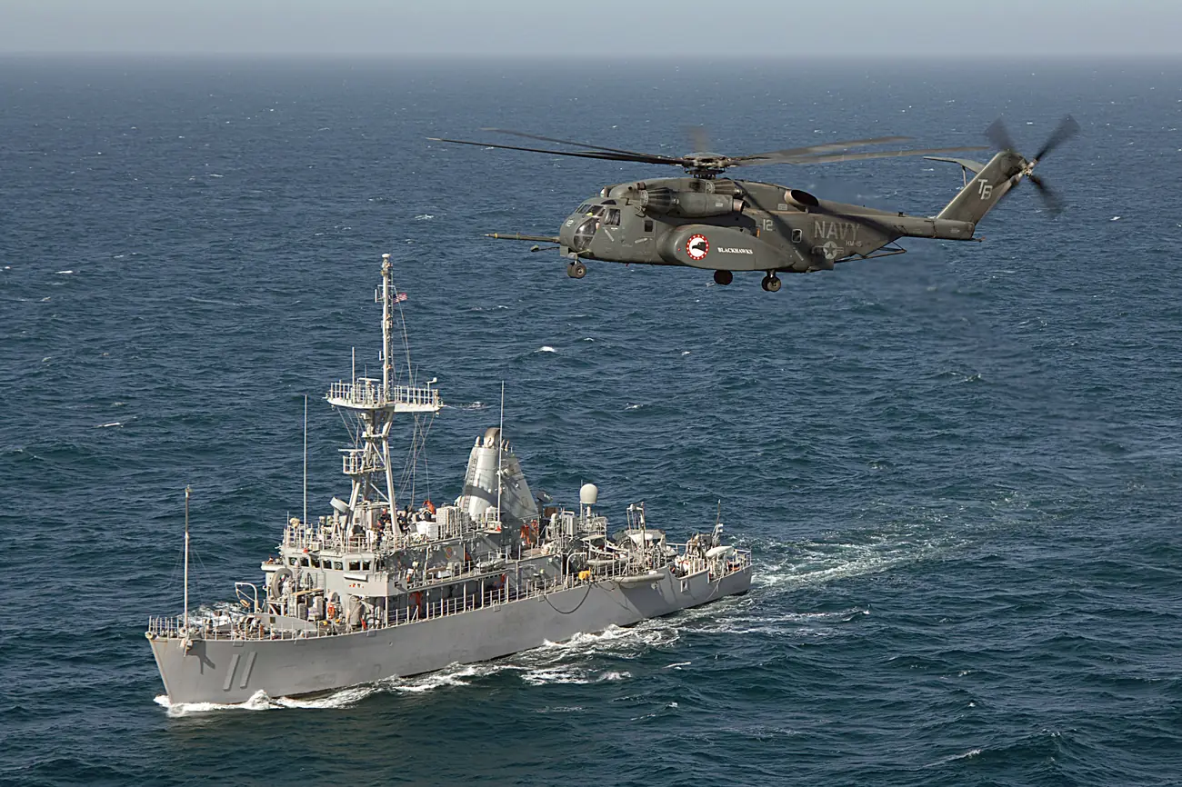 An Avenger-class minesweeper with a Sea Dragon helicopter overhead