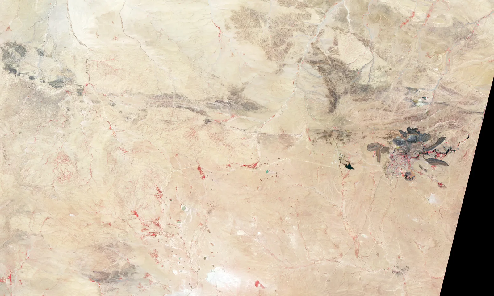 False-color satellite view of the Bayan Obo mining district in Inner Mongolia, China, showing circular open pits and green tailings ponds against bare tan terrain