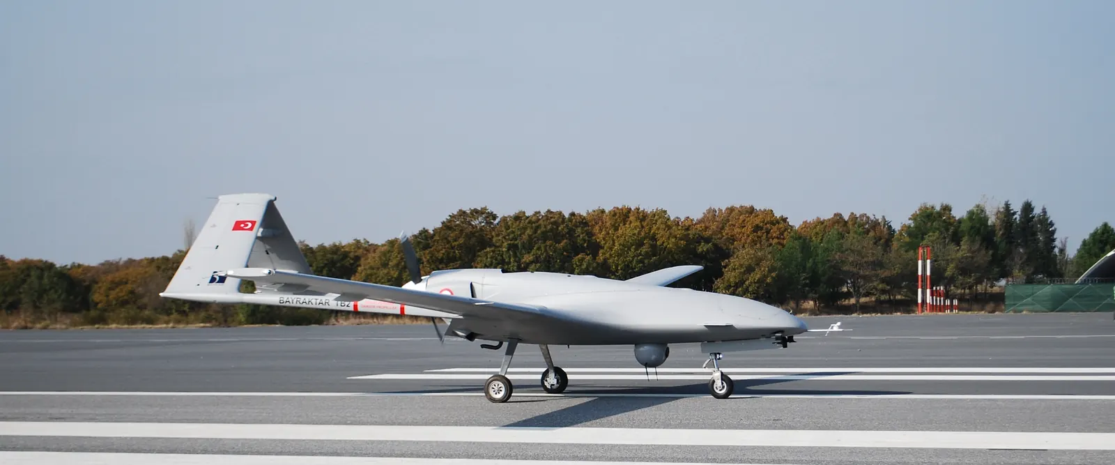 A Bayraktar TB2 armed drone on a runway, with a Turkish flag on its tail and munitions under its wings