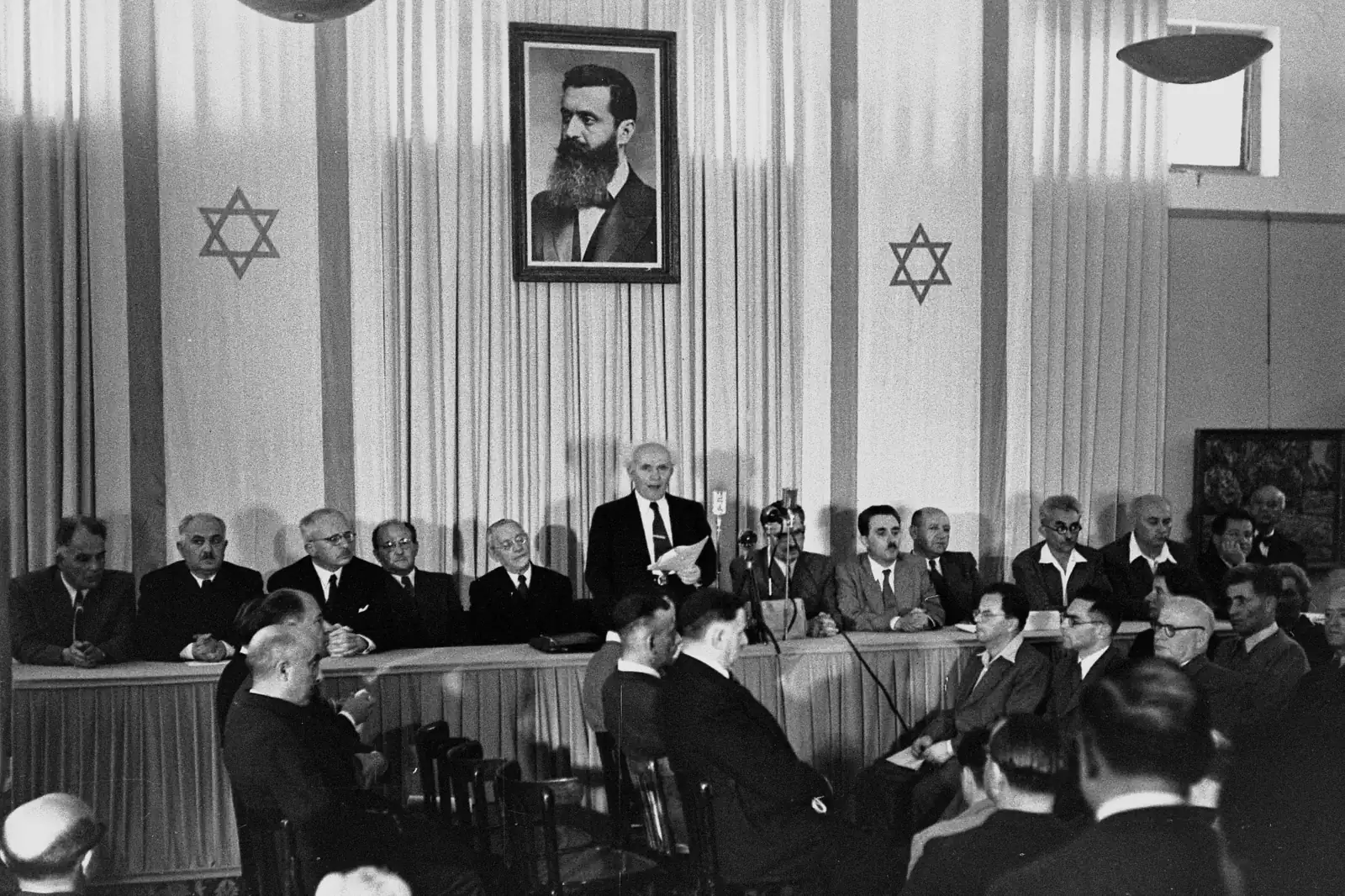 David Ben-Gurion reading Israel's declaration of independence beneath a portrait of Theodor Herzl in Tel Aviv on May 14, 1948