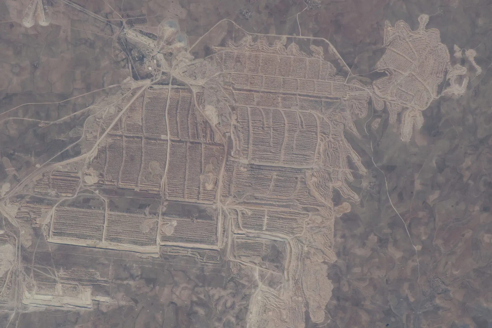 Satellite view of the Bou Craa phosphate mine in Western Sahara, showing the mine's white open pit and a conveyor belt stretching northwest toward the Atlantic coast
