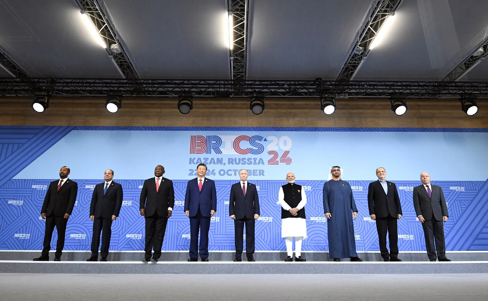 Nine national leaders and officials stand in a row on a stage in front of a blue backdrop reading BRICS 2024 Kazan Russia