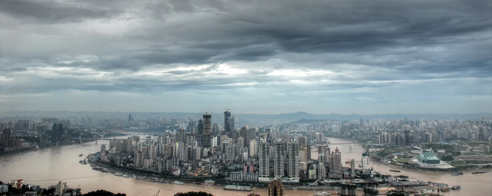 Panoramic view of the Chongqing skyline from Nanshan, with hundreds of apartment towers and office blocks crowding both banks of the Yangtze River under heavy clouds