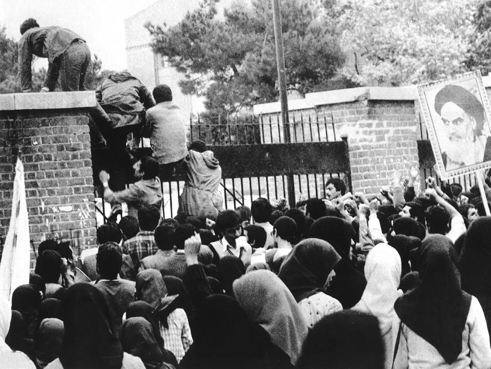 Iranian students climbing the gates of the US Embassy in Tehran on November 4, 1979, a crowd massed below