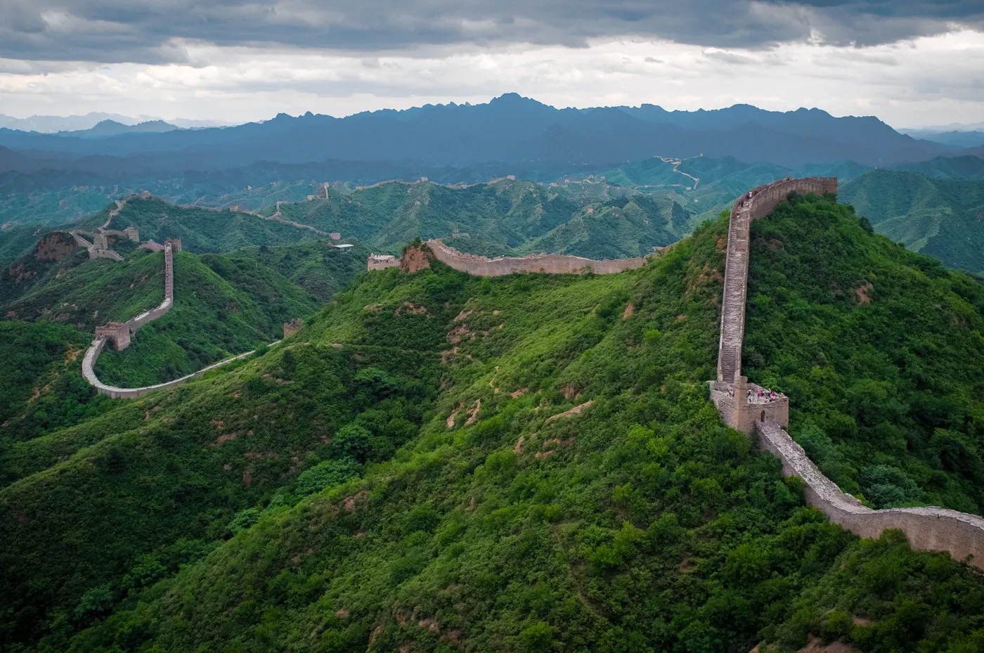 The Great Wall of China winding across forested mountain ridges at Jinshanling, disappearing into mist