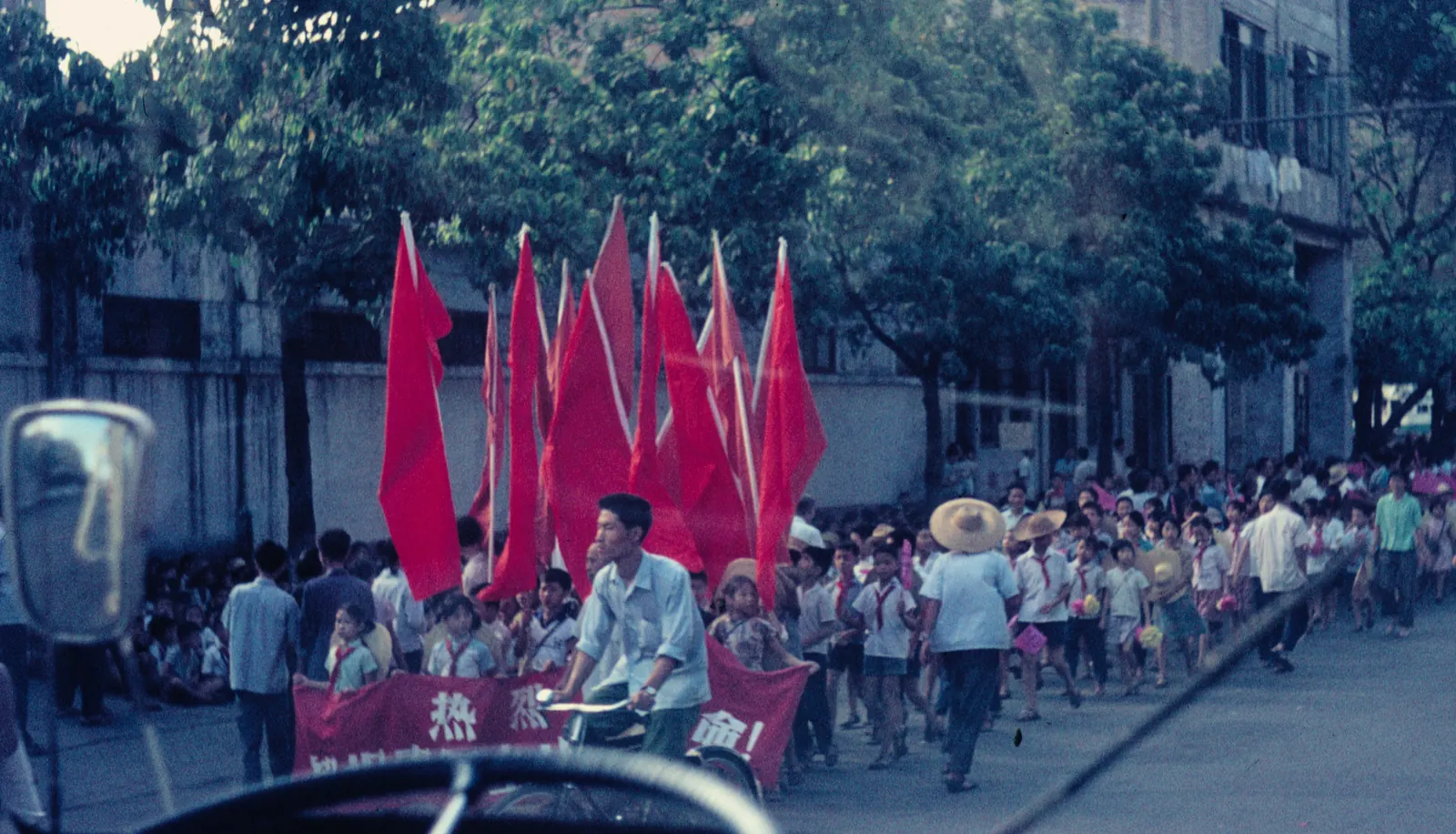 A parade of young people carrying red flags and Mao portraits through a street in Guangzhou during the Cultural Revolution