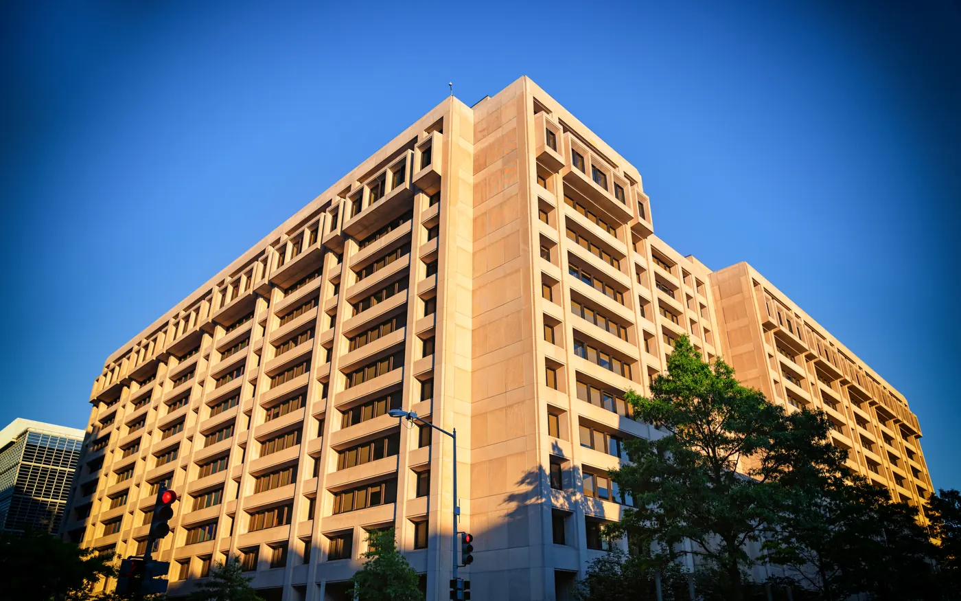 The IMF headquarters building in Washington, DC, a large brutalist office block photographed from below against a blue sky