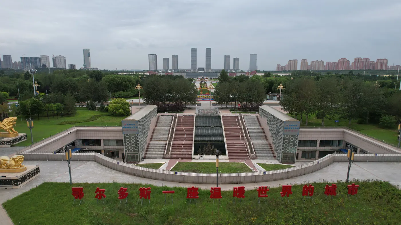 Aerial view of Kangbashi district in Ordos, showing the Ordos Museum in the foreground with empty plazas and residential apartment towers on the skyline