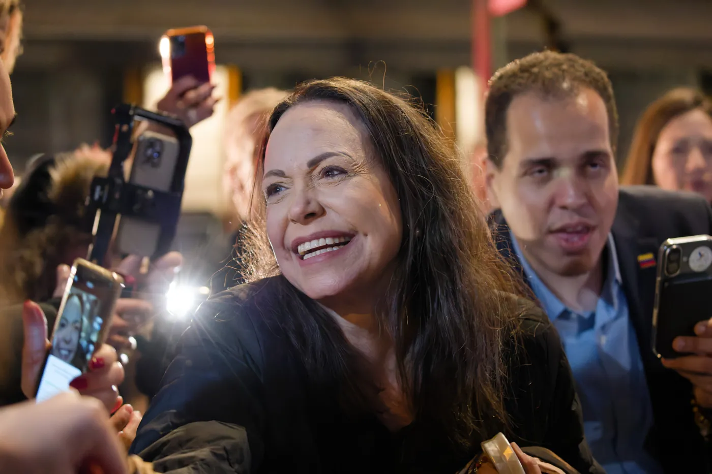 María Corina Machado reaching out to a crowd of supporters holding Venezuelan flags