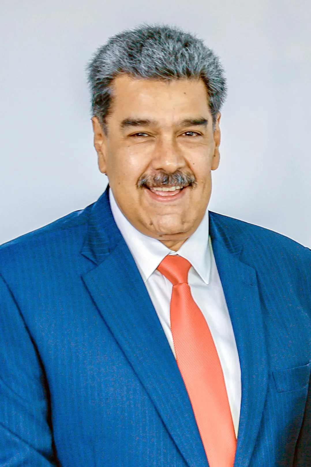 Nicolás Maduro standing in a suit in front of a wooden wall