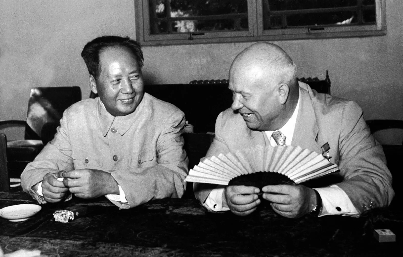 Mao Zedong and Nikita Khrushchev laughing together at a table during Khrushchev's visit to Beijing in 1958