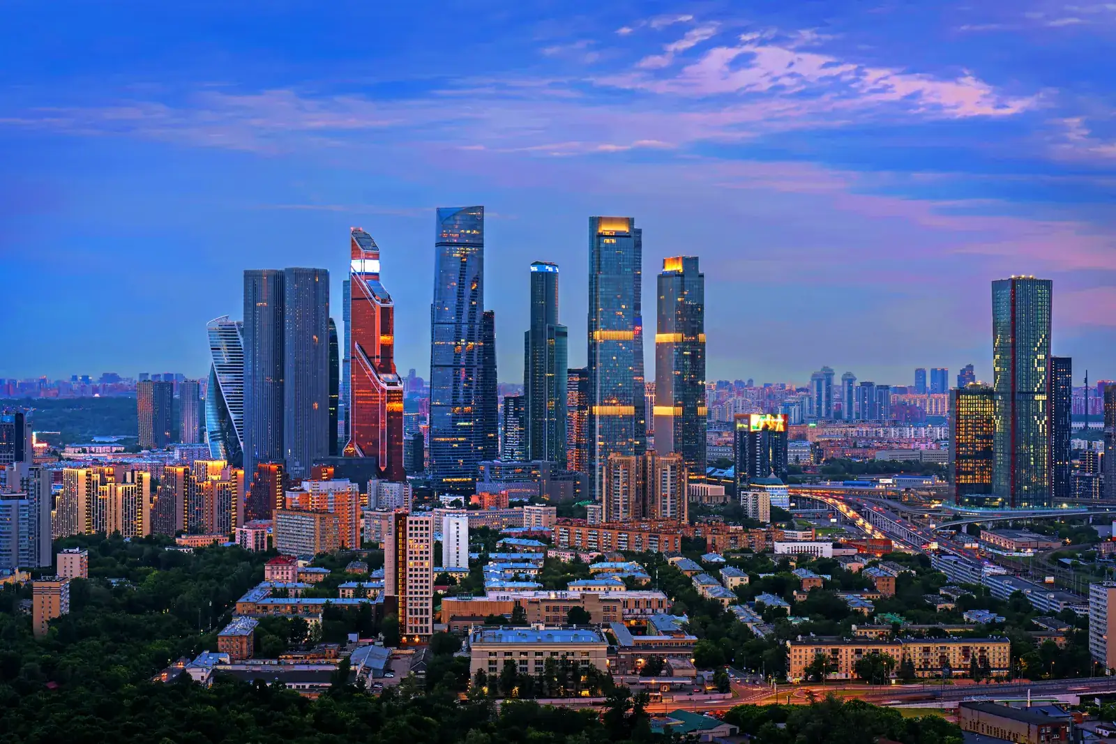 The Moscow International Business Center skyline at twilight, with glass skyscrapers lit up against a darkening sky