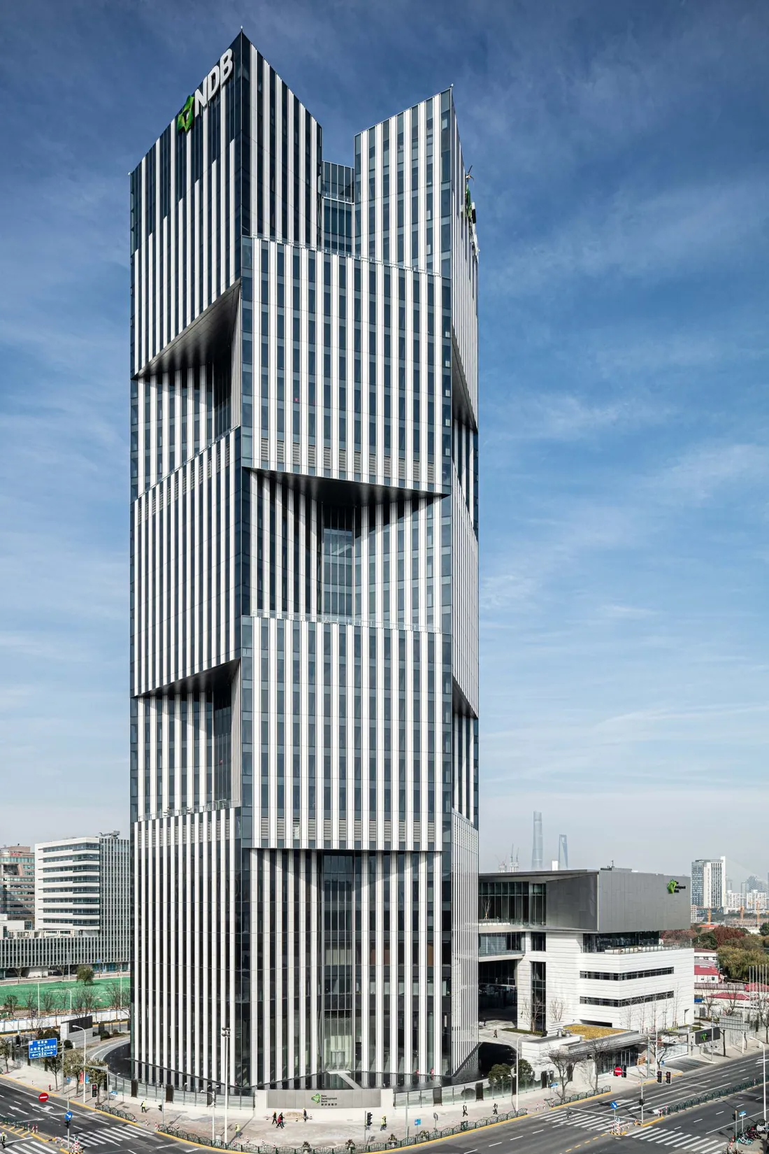 The New Development Bank's angular glass tower in Shanghai, seen from street level against a blue sky