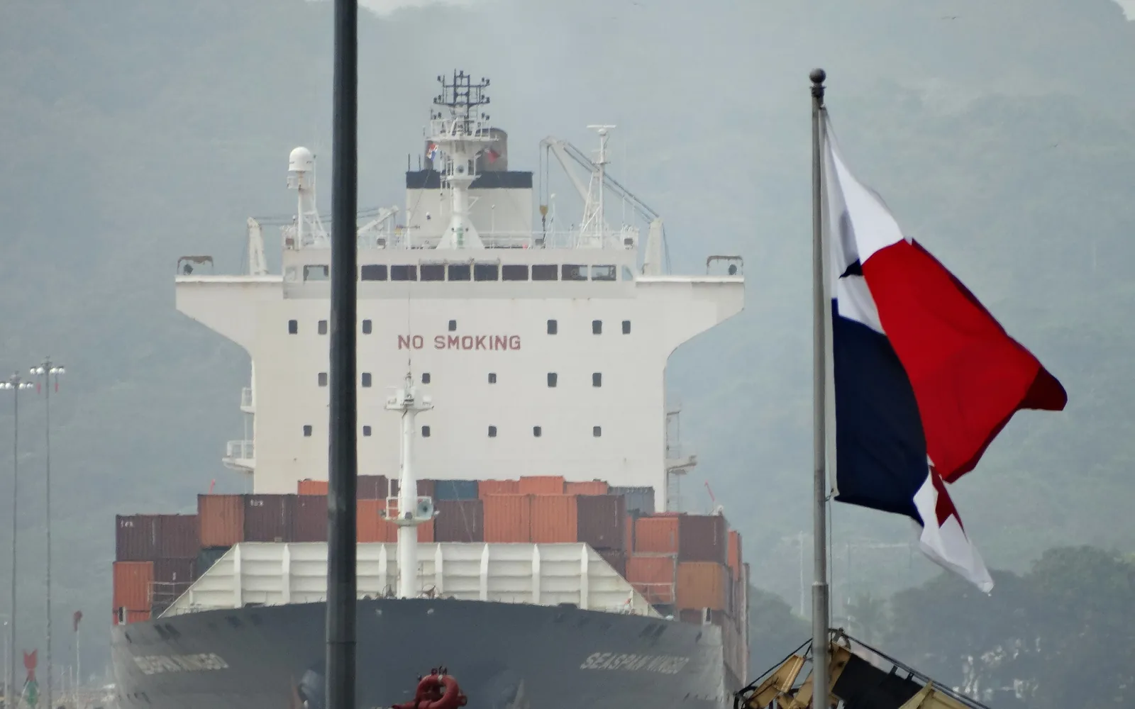 A container ship entering the Miraflores locks of the Panama Canal, with the Panamanian flag flying in the foreground