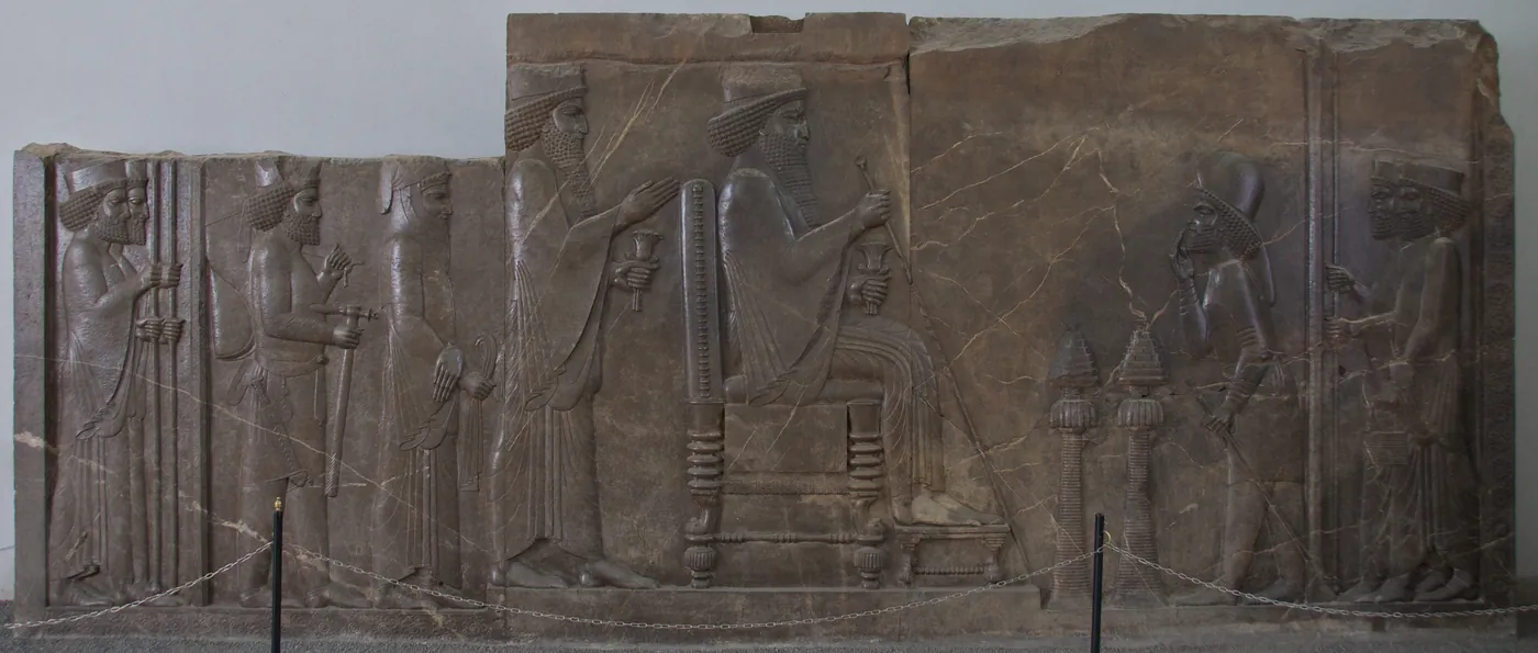 Stone relief of a Persian king seated on a throne, holding a staff, with attendants behind him