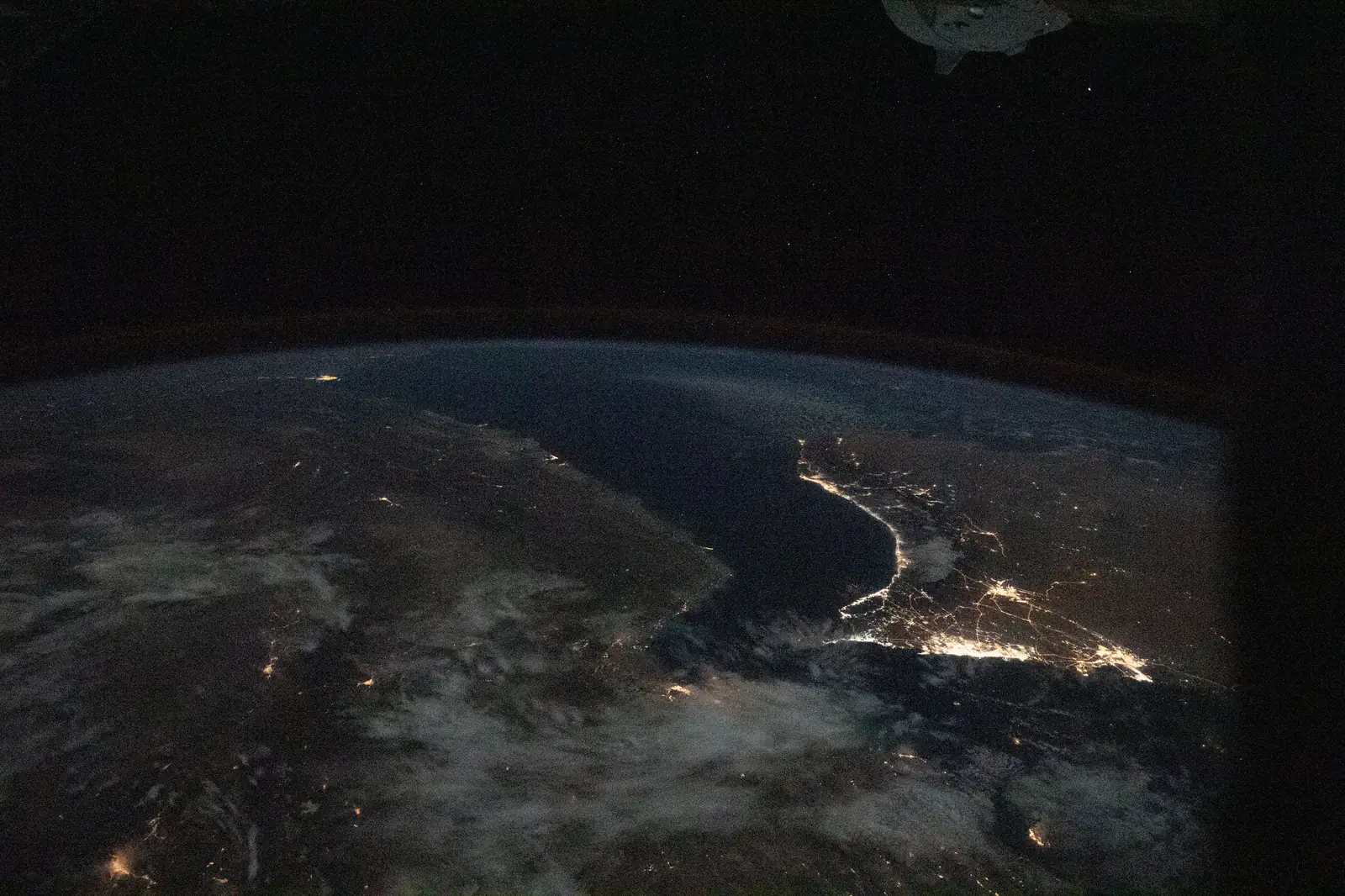 The Persian Gulf at night seen from the International Space Station, with city lights tracing the coastlines of Iran to the north and Saudi Arabia to the south