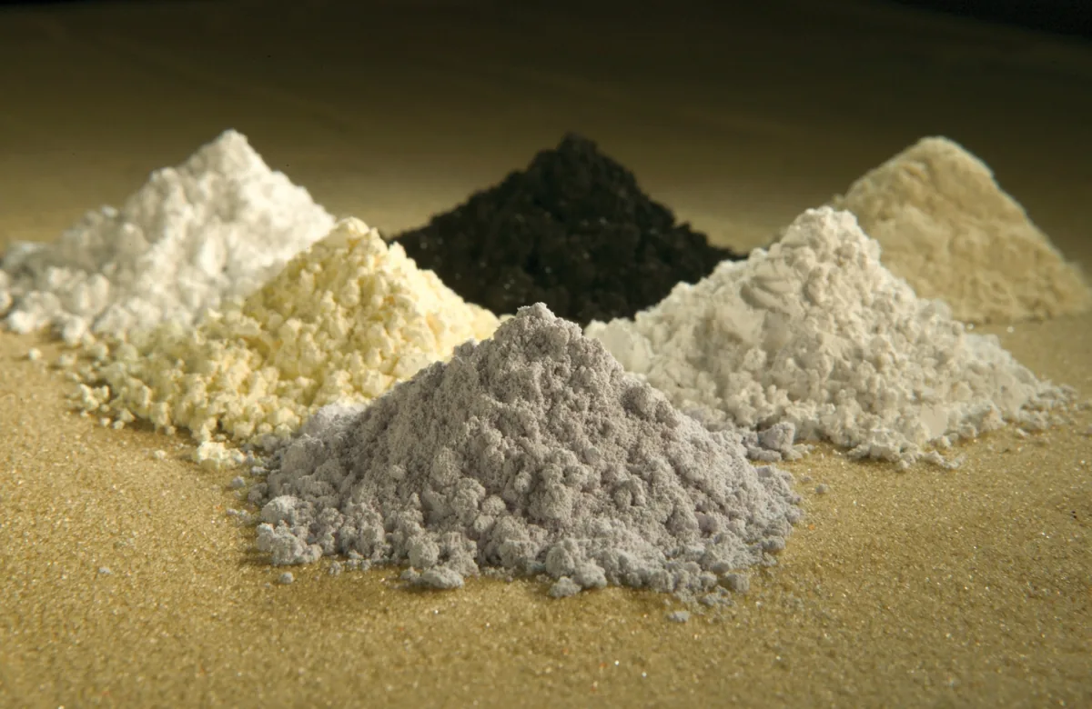Small piles of differently colored rare-earth oxide powders on a dark surface