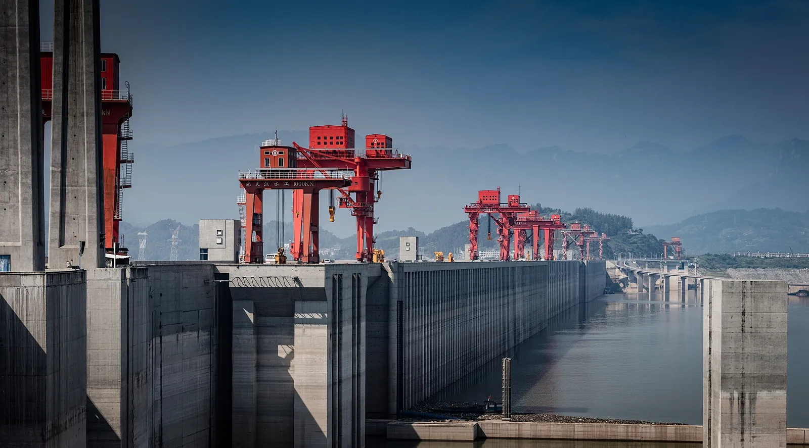 The Three Gorges Dam on the Yangtze River in Hubei province, China, with red gantry cranes lining the top of the massive concrete dam wall