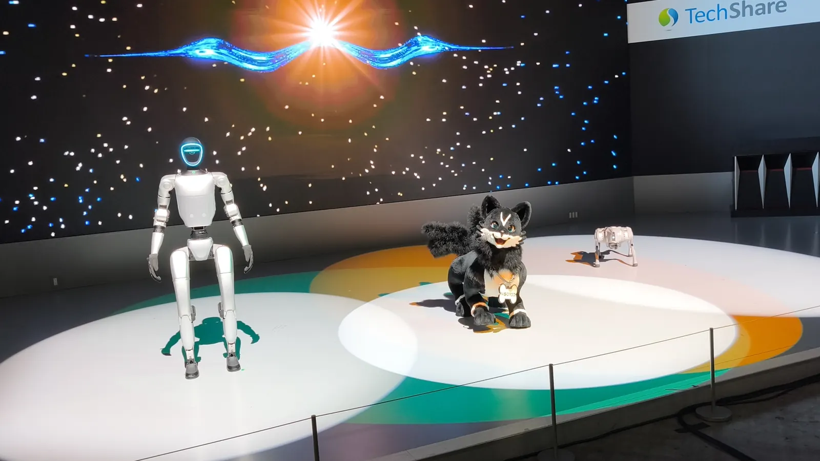 A Unitree G1 humanoid robot, a fox-shaped animoid, and a Go2 quadruped robot on a lit stage at the Japan Mobility Show 2025