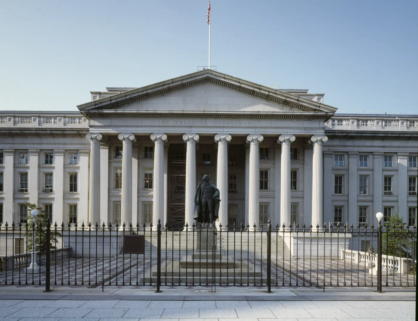 The neoclassical facade of the US Treasury Department building in Washington, with Ionic columns and the statue of Alexander Hamilton in front
