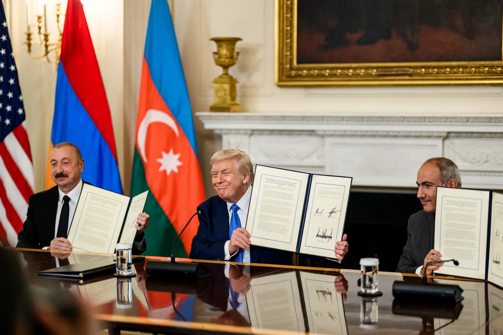 Ilham Aliyev, Donald Trump and Nikol Pashinyan hold up signed documents at a table in front of Armenian and Azerbaijani flags