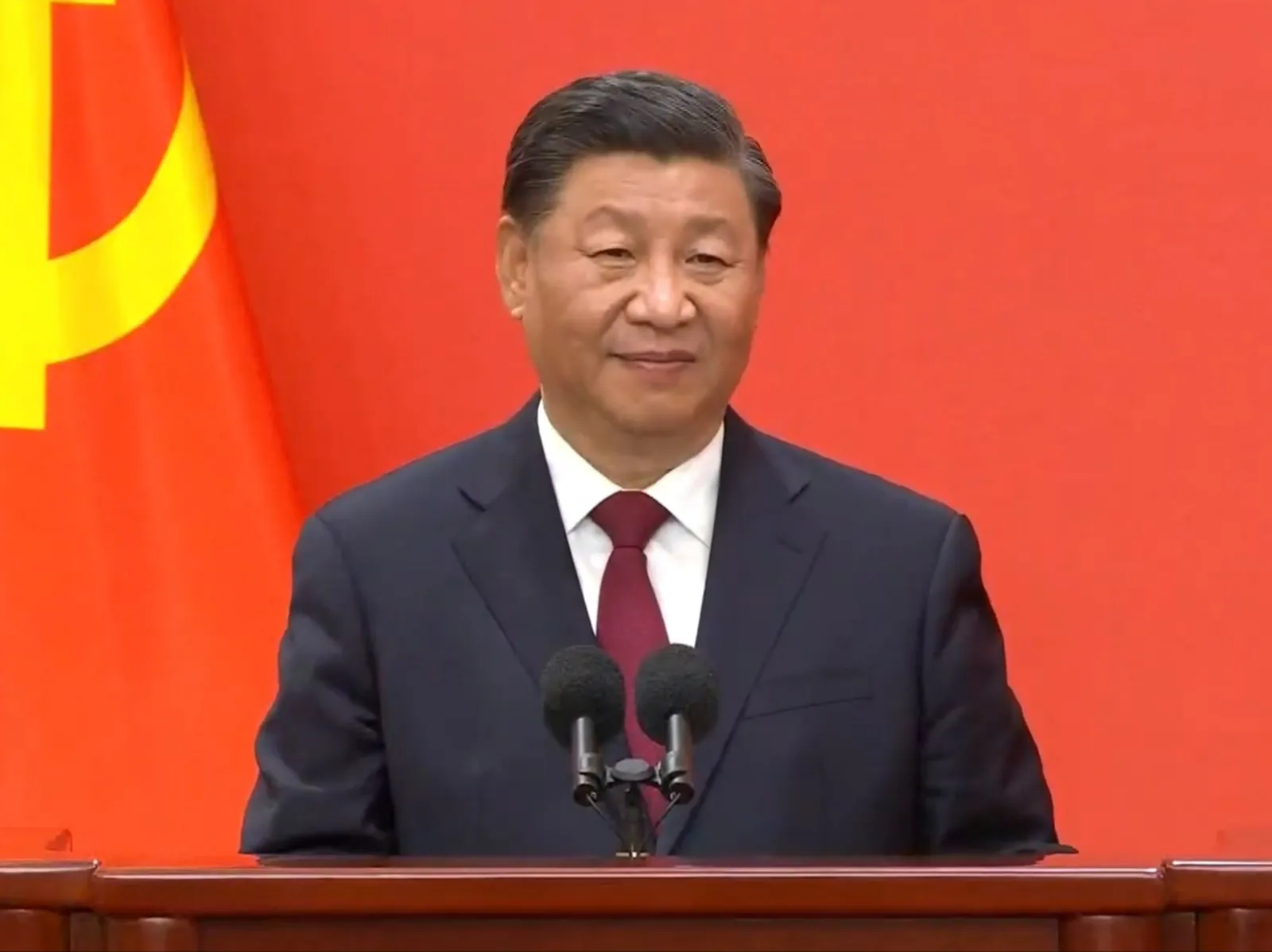 Xi Jinping speaking at a podium in front of a red backdrop at the Great Hall of the People