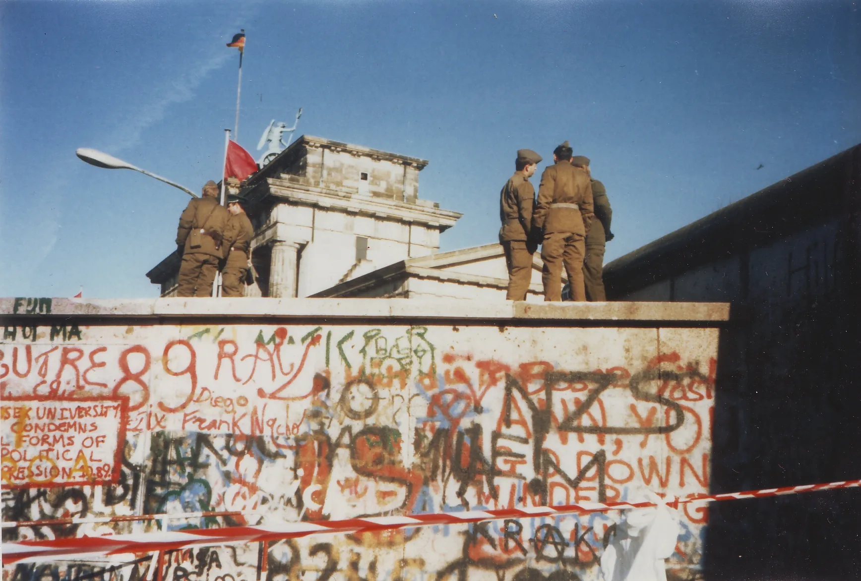 East German border guards standing on top of the graffiti-covered Berlin Wall in front of the Brandenburg Gate, November 16, 1989