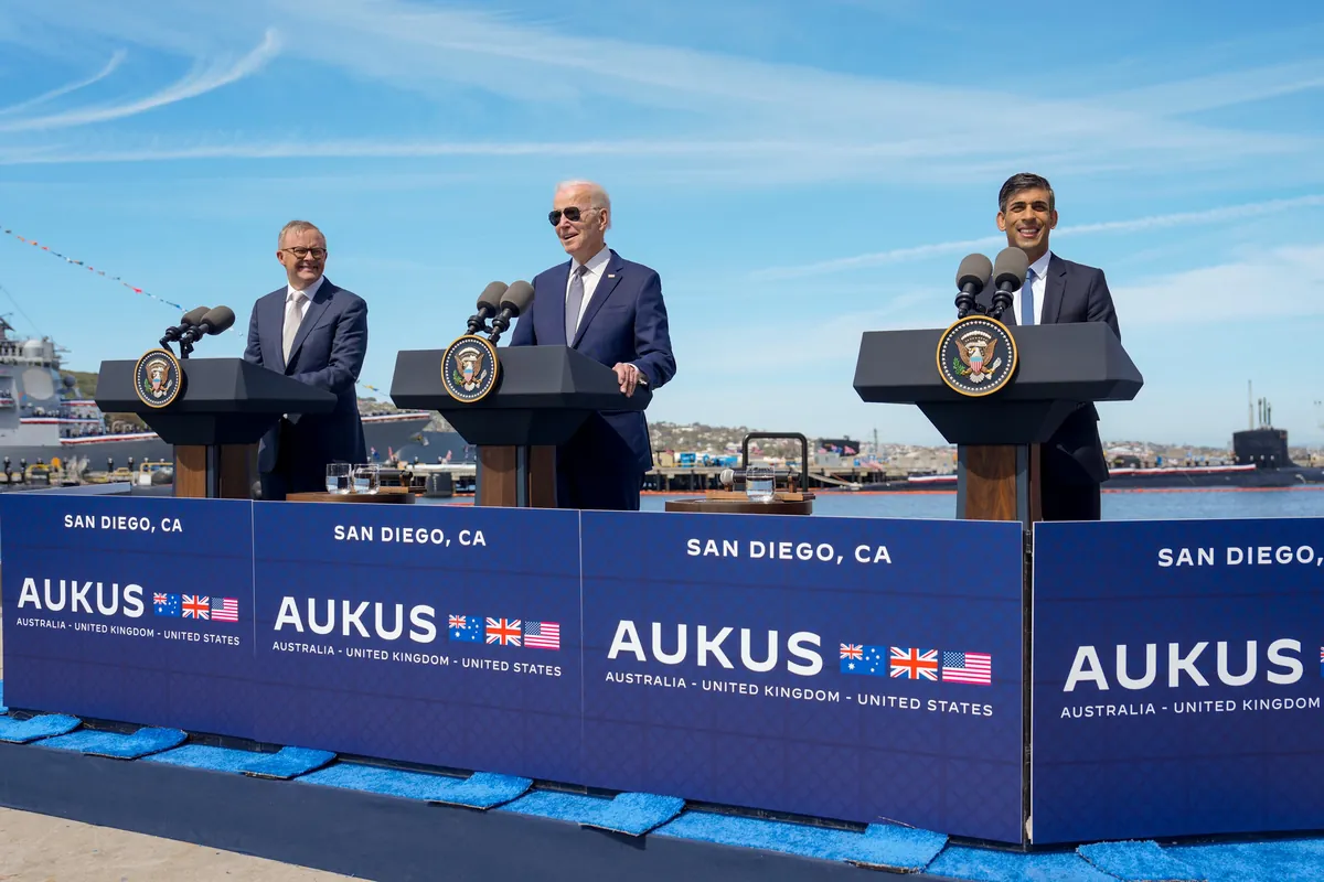 Anthony Albanese, Joe Biden and Rishi Sunak stand at three lecterns on a pier in San Diego, behind a blue banner reading AUKUS, with a submarine in the harbor behind them