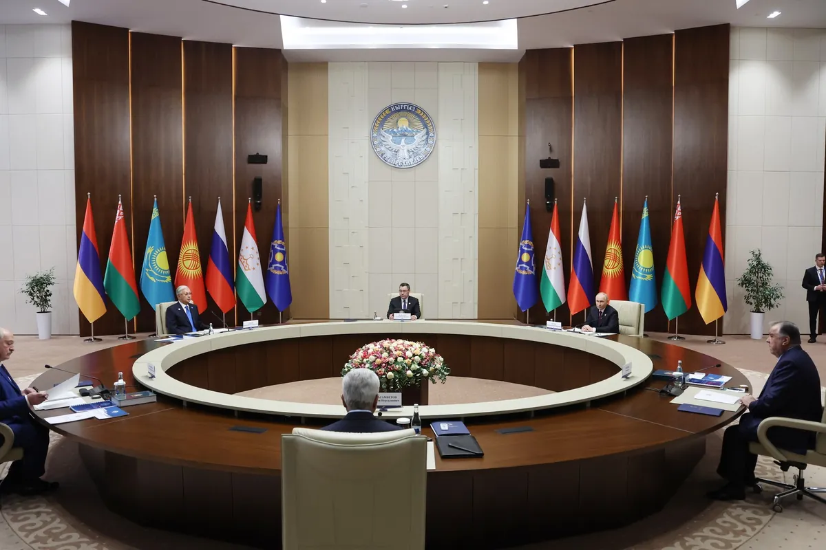 Leaders sit around a large round table in a hall in Bishkek, in front of two rows of flags of the CSTO's six members and of the CSTO itself