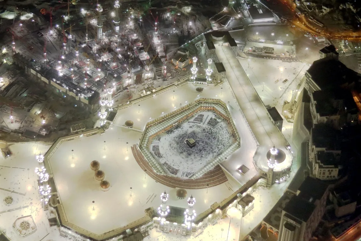 The Great Mosque of Mecca at night, seen from above, with crowds of pilgrims around the Kaaba in its floodlit courtyard