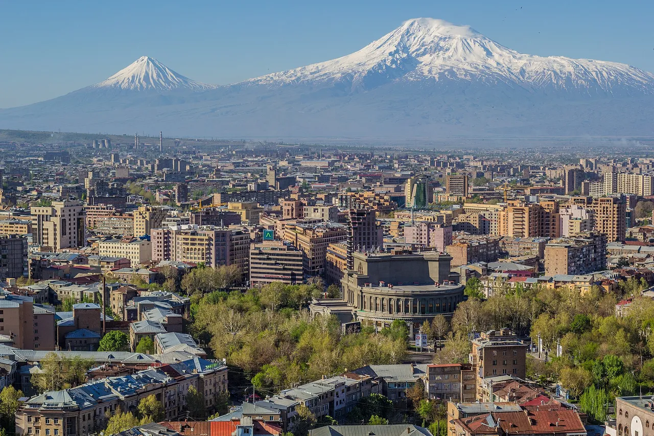 Mount Ararat, snow-covered, rises behind the rooftops of Yerevan, with the round Opera house in the center