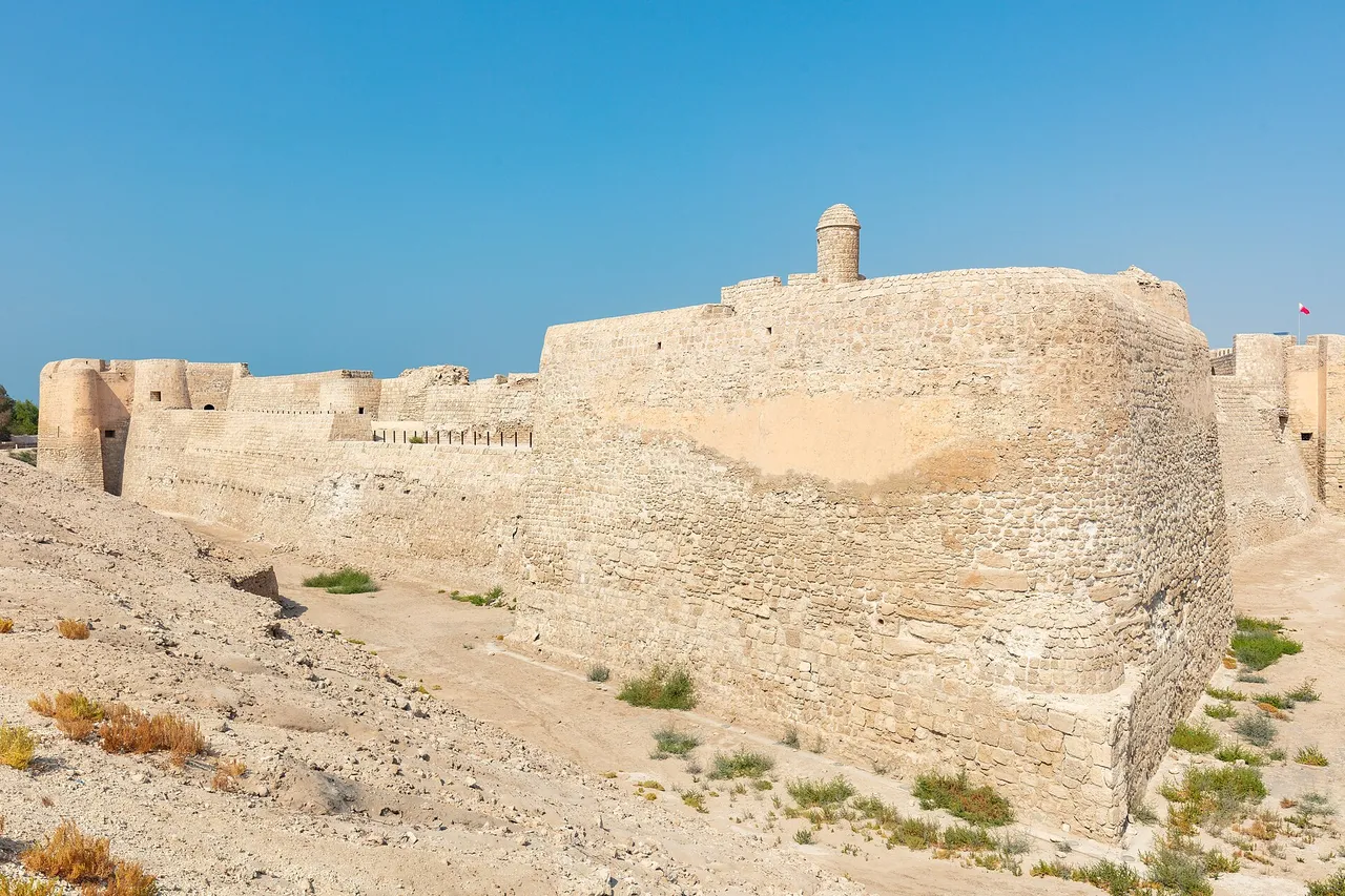 The stone walls and round tower of Qal'at al-Bahrain, an old fort on a low mound, under a clear blue sky