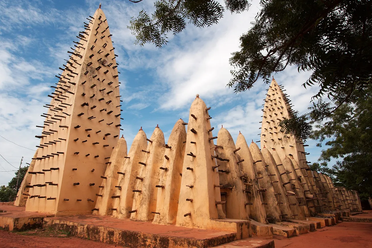 The Grand Mosque of Bobo-Dioulasso, a sand-colored mud-brick building with two tall cone-shaped towers and rows of smaller cones, studded with wooden beams, under a blue sky