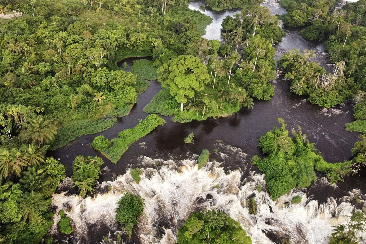 Aerial view of the Lobé Falls, white water tumbling over rocks between islands of thick green rainforest
