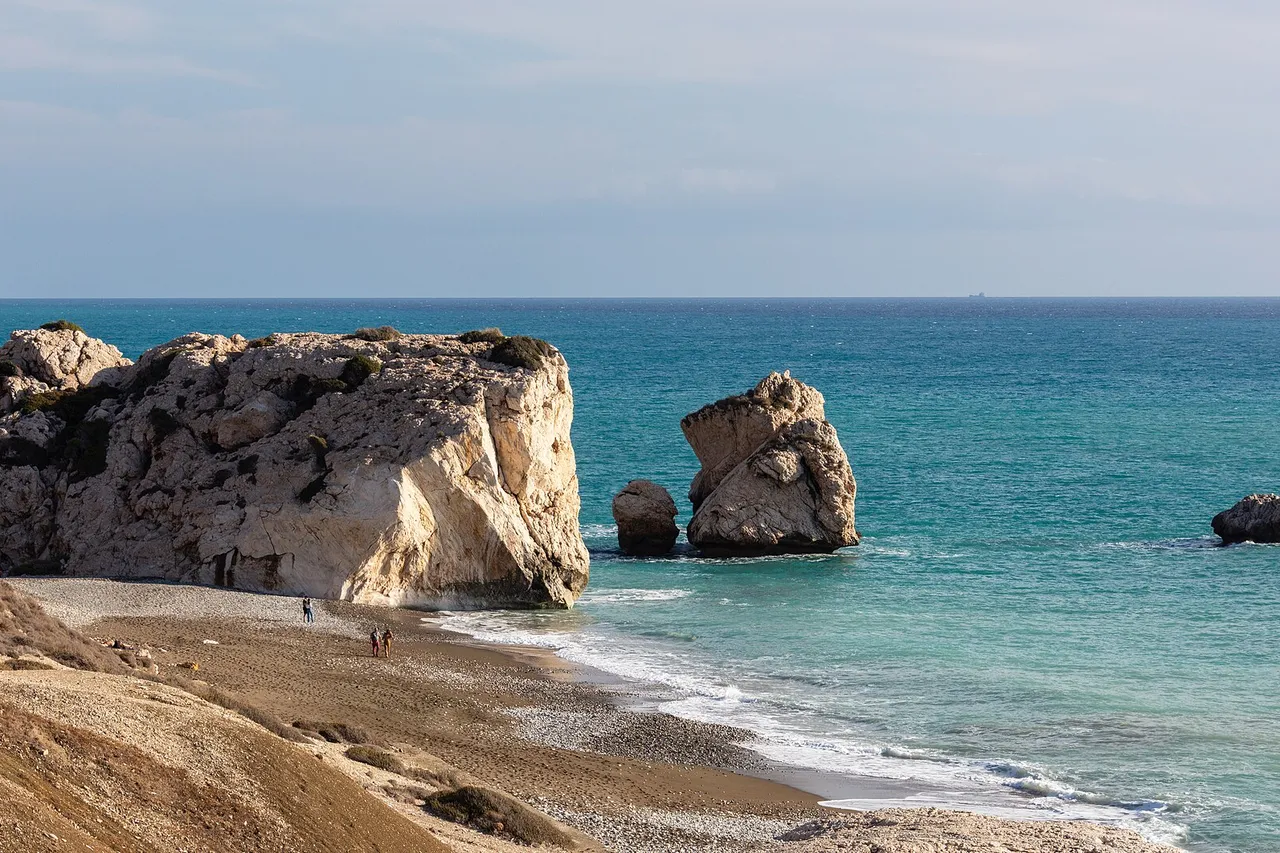 Large pale rocks rise from a turquoise sea beside a curving pebble beach