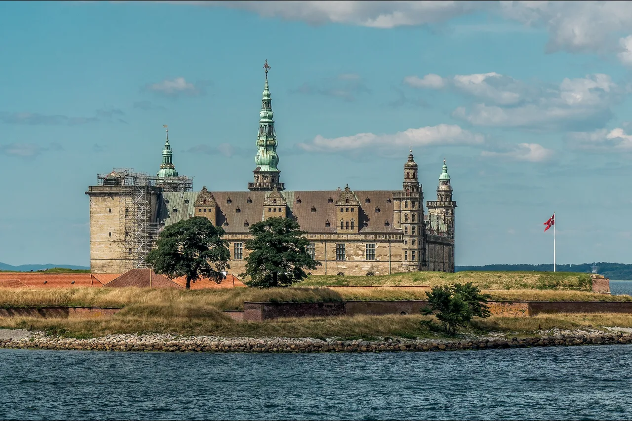 Kronborg Castle, with green copper spires and red brick ramparts, seen across the water of the Øresund strait