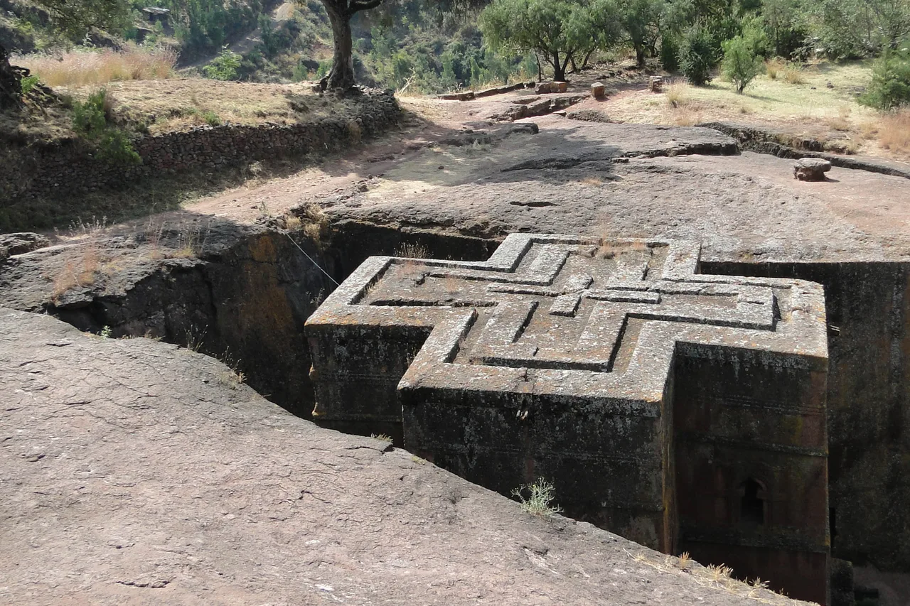 The Church of Saint George in Lalibela, carved down into the rock in the shape of a cross, with trees and hills behind
