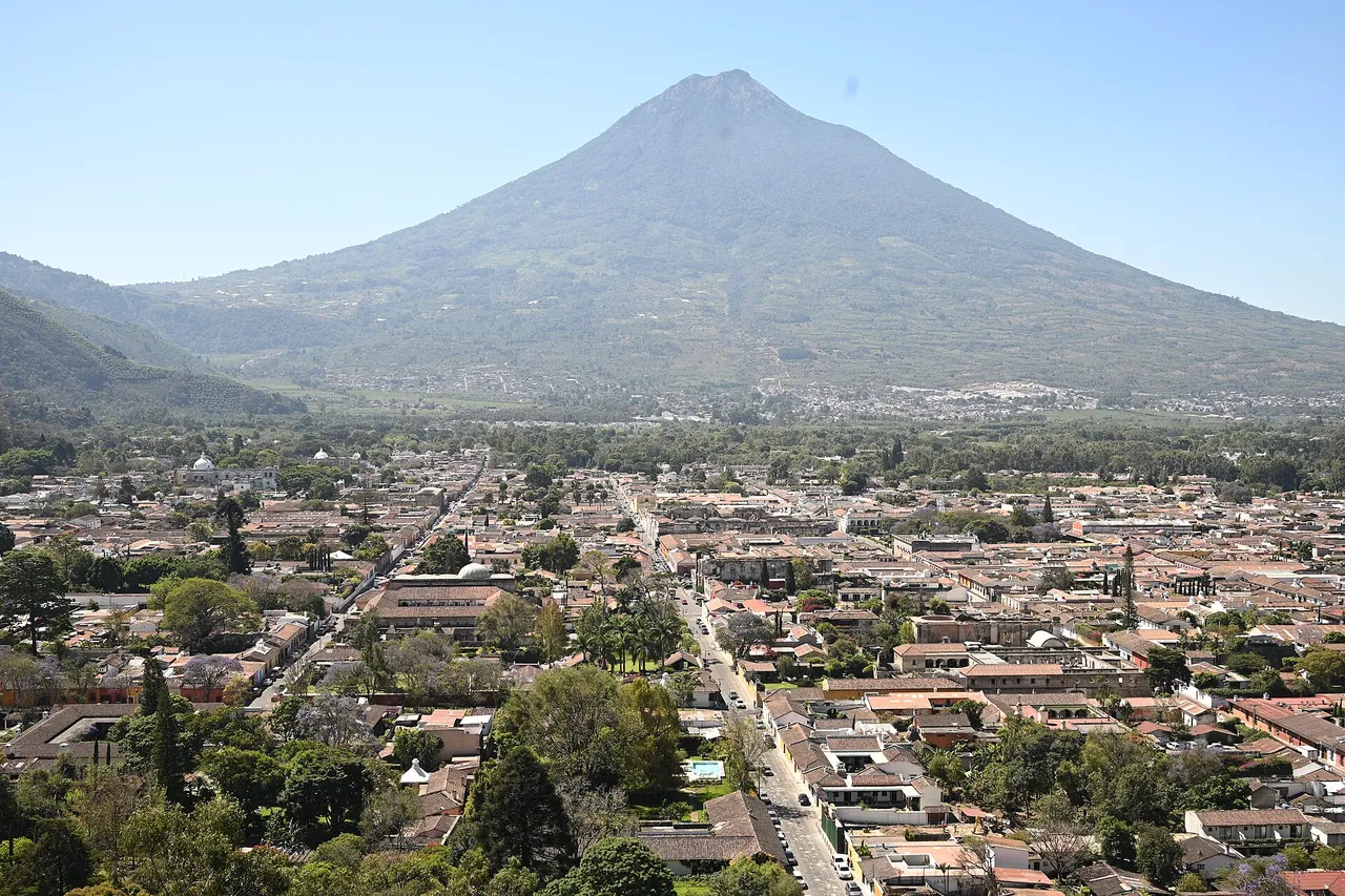 The low tiled roofs and church domes of Antigua Guatemala spread across a green valley below the tall cone of the Volcán de Agua