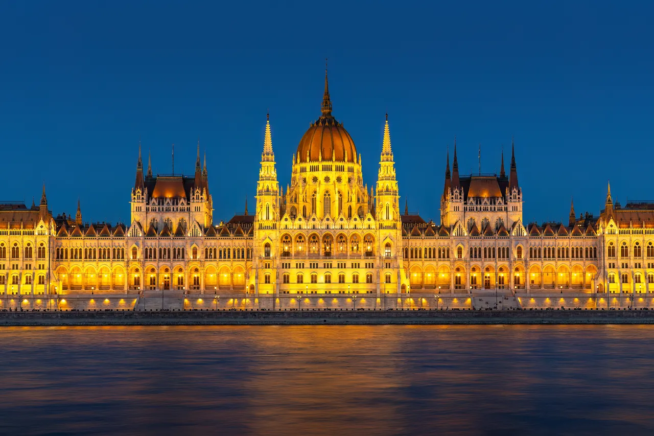 The Hungarian Parliament Building in Budapest, lit up at dusk, seen across the Danube
