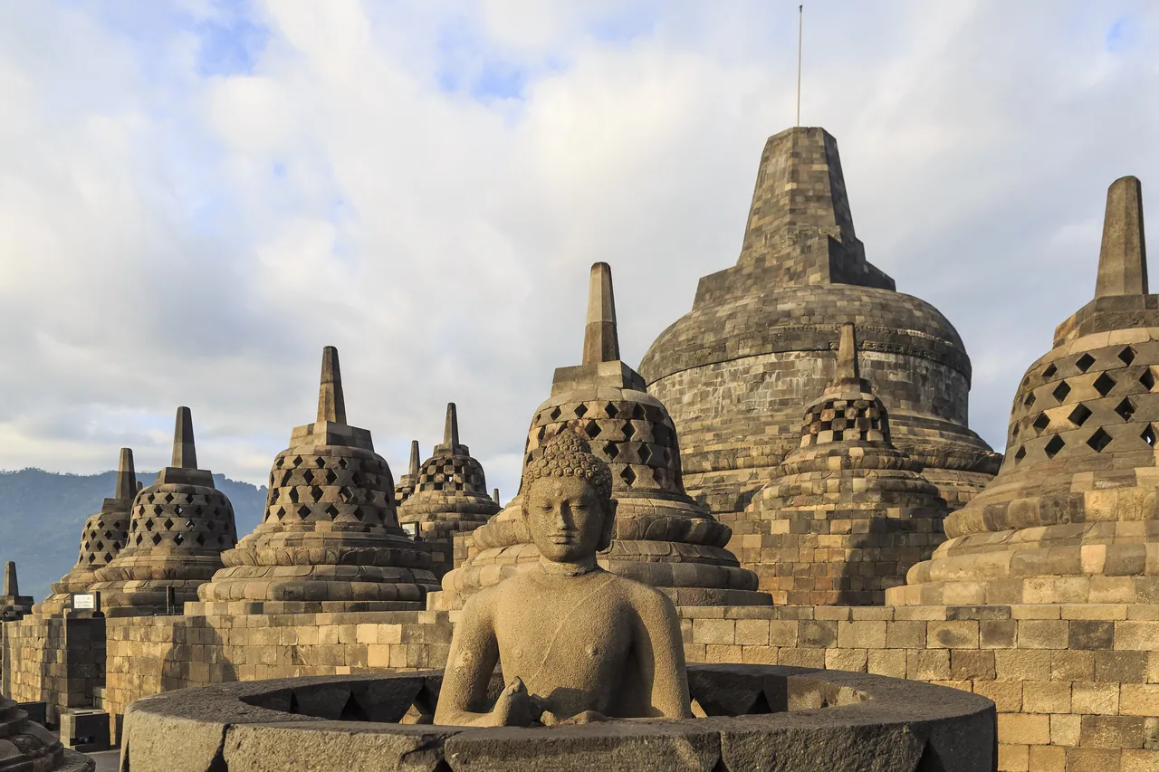 A stone Buddha seated among the bell-shaped stupas on the upper terrace of Borobudur temple in Central Java