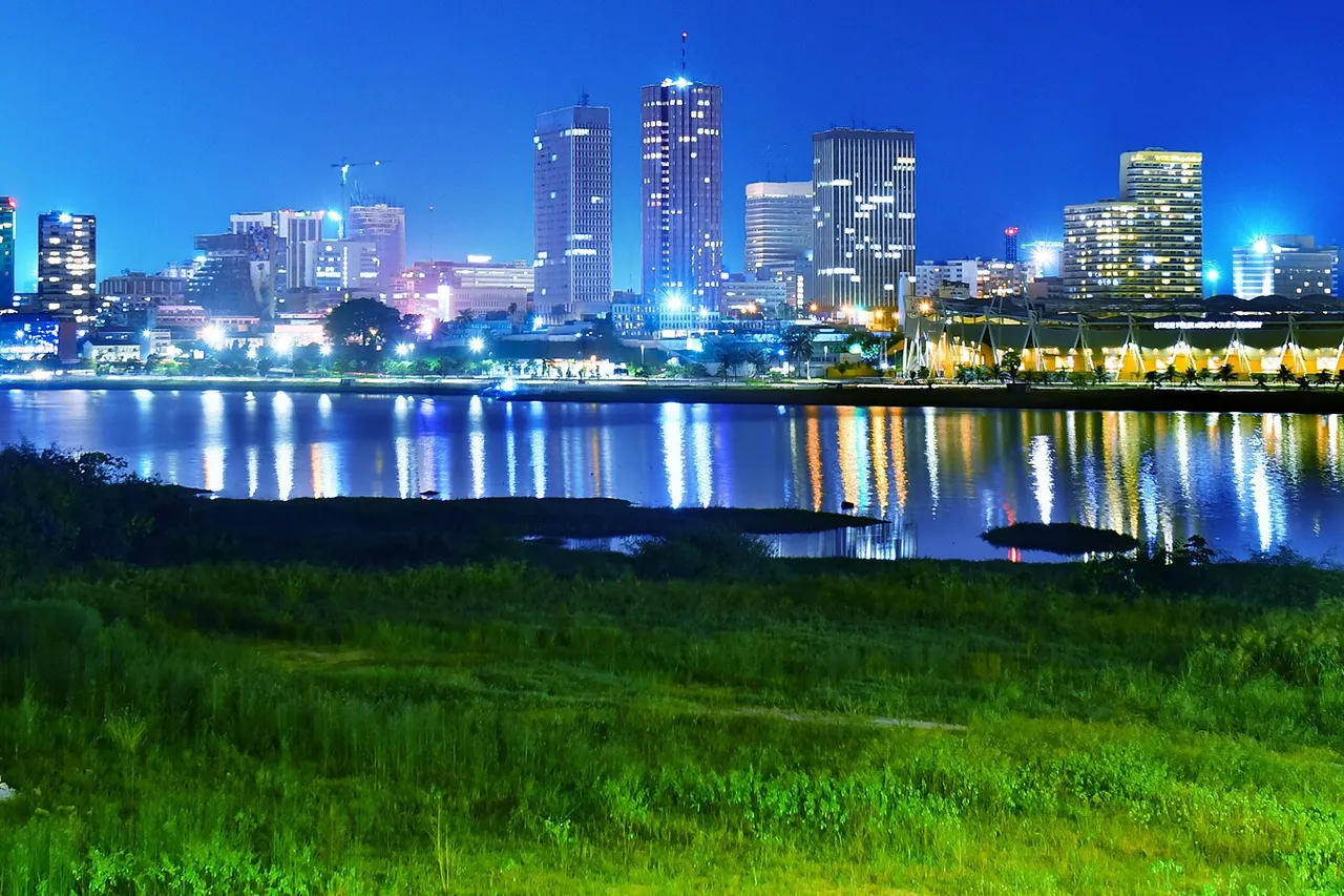 The towers of Abidjan's Plateau business district lit up at night and reflected in the lagoon, with grass in the foreground