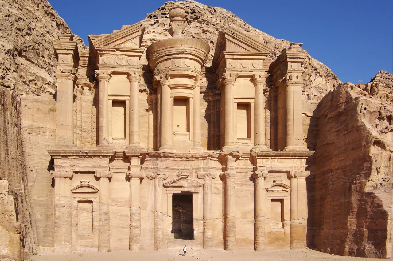 The Monastery, a tall temple facade carved into pink sandstone cliffs at Petra, under a clear blue sky
