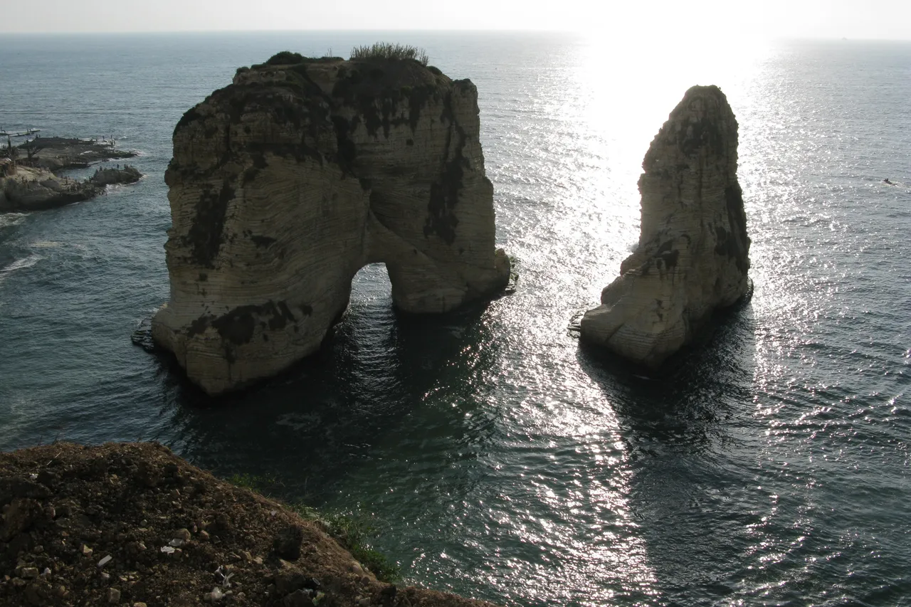 The two Pigeon Rocks, one with a natural arch, stand in the Mediterranean Sea off the Beirut coast, with the sun glittering on the water