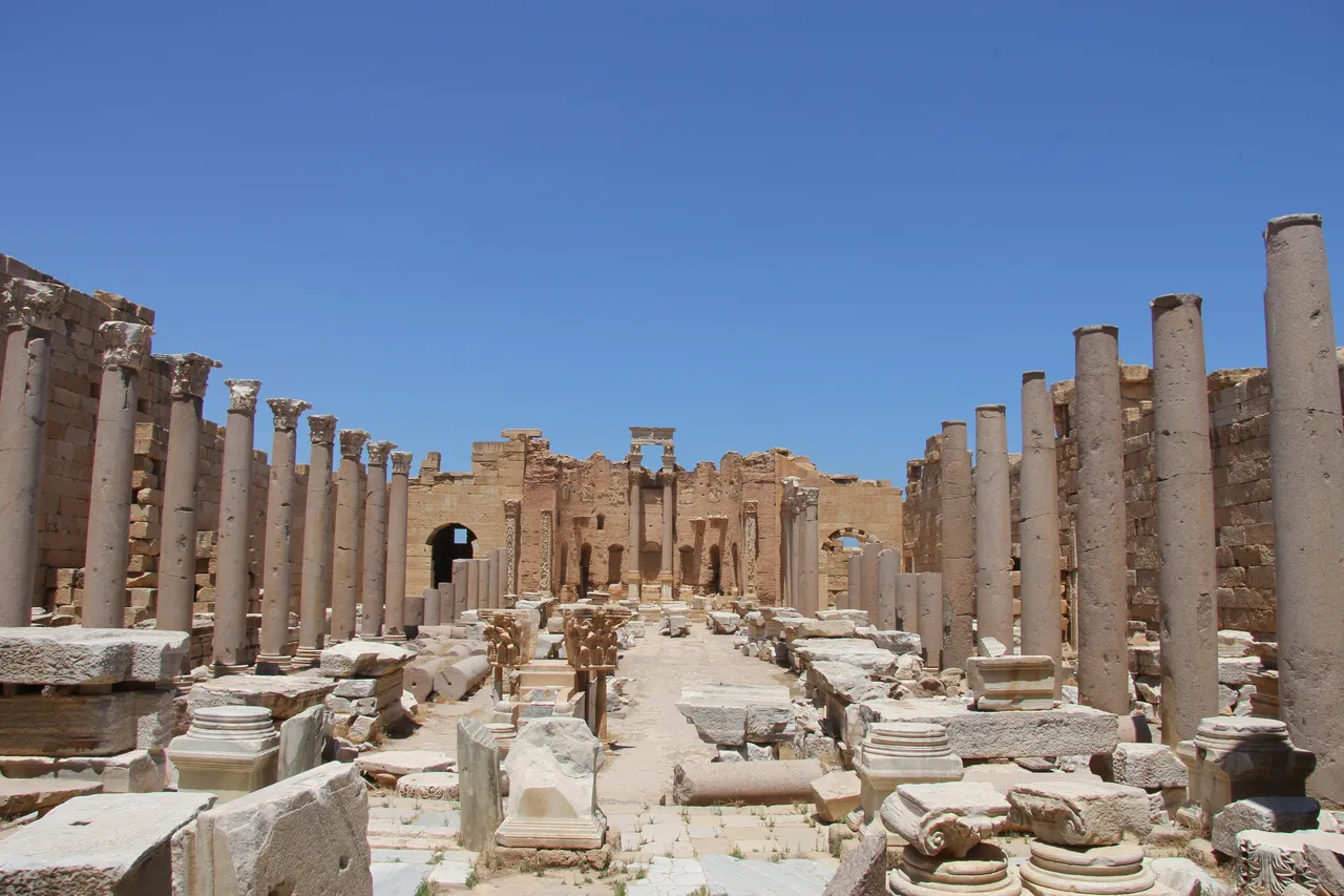 Rows of tall stone columns line a ruined Roman basilica under a deep blue sky at Leptis Magna