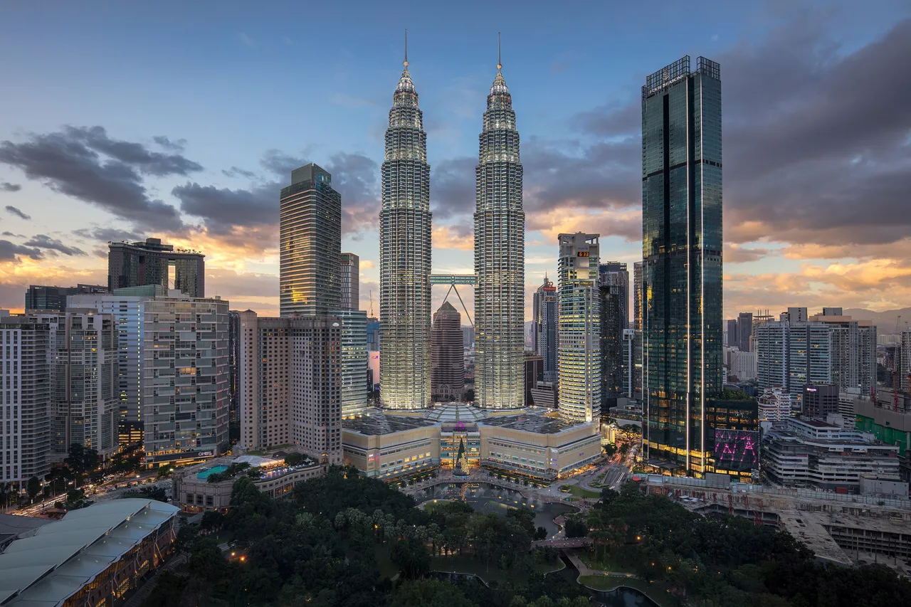 The twin Petronas Towers lit up at dusk above the high-rise buildings and park of central Kuala Lumpur
