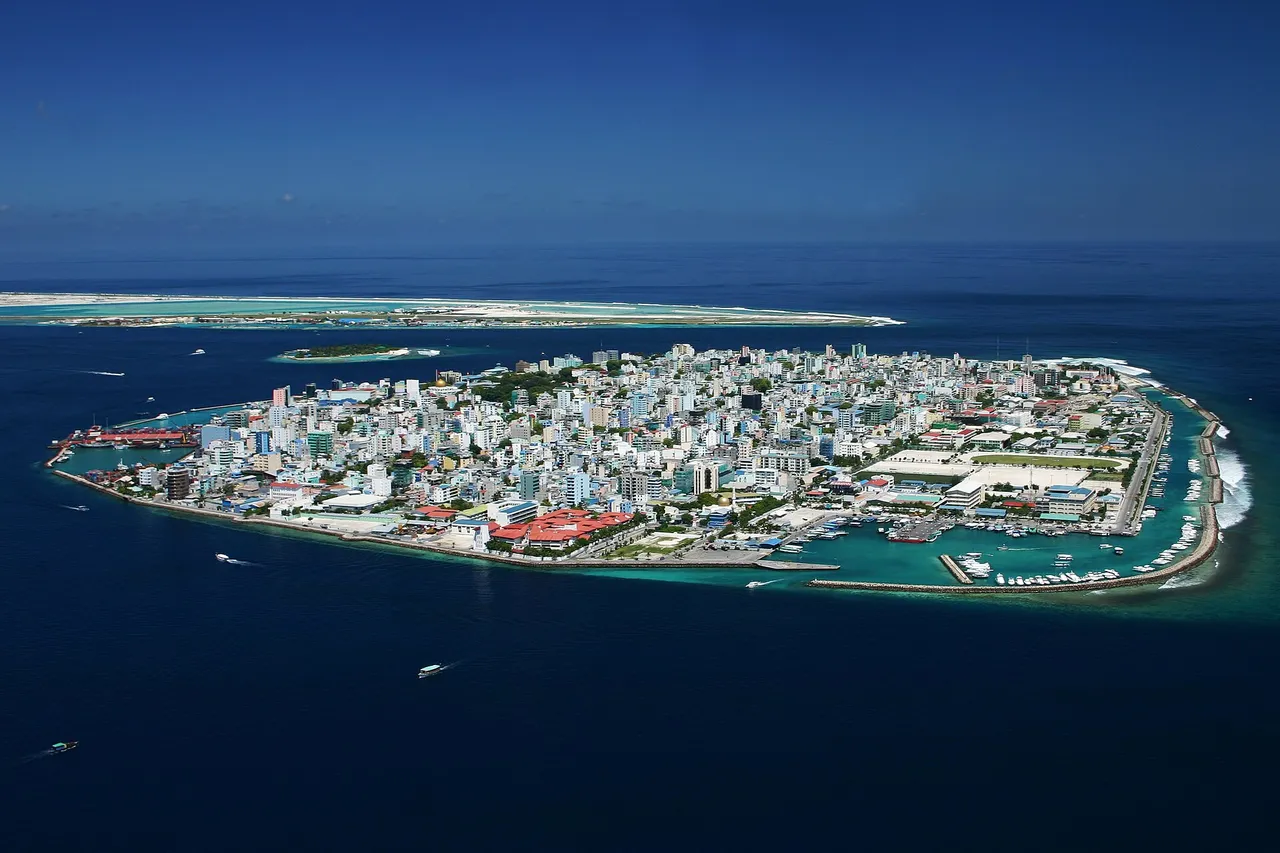 Aerial view of a small flat island covered edge to edge with white buildings and harbors, surrounded by deep blue sea