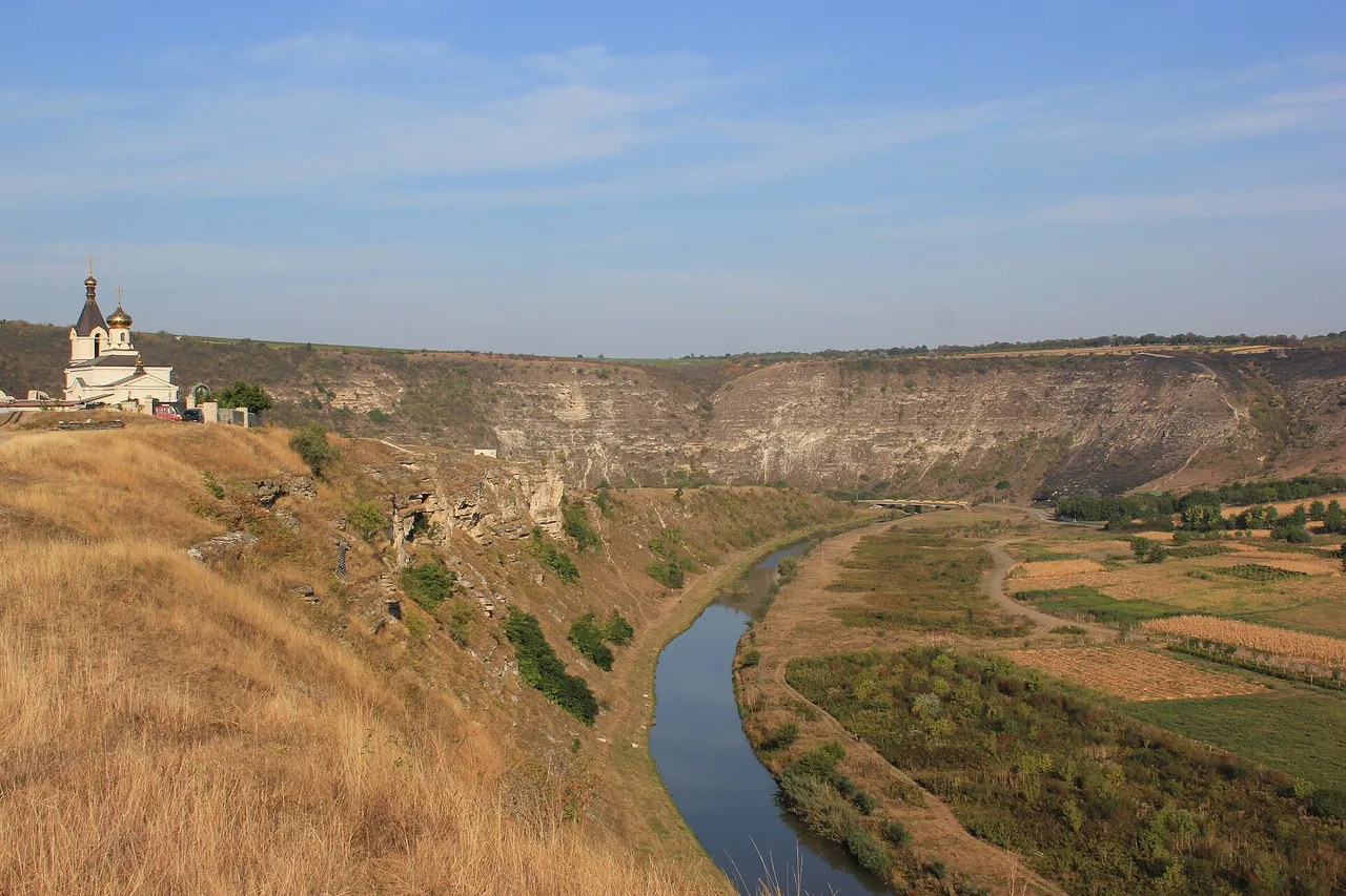 A small white church with a golden dome on a cliff above a winding river in a deep, dry gorge